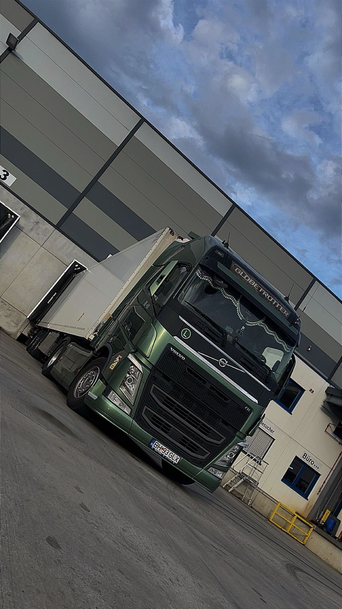 Camion verde la un doc de încărcare, sub un cer înnorat.